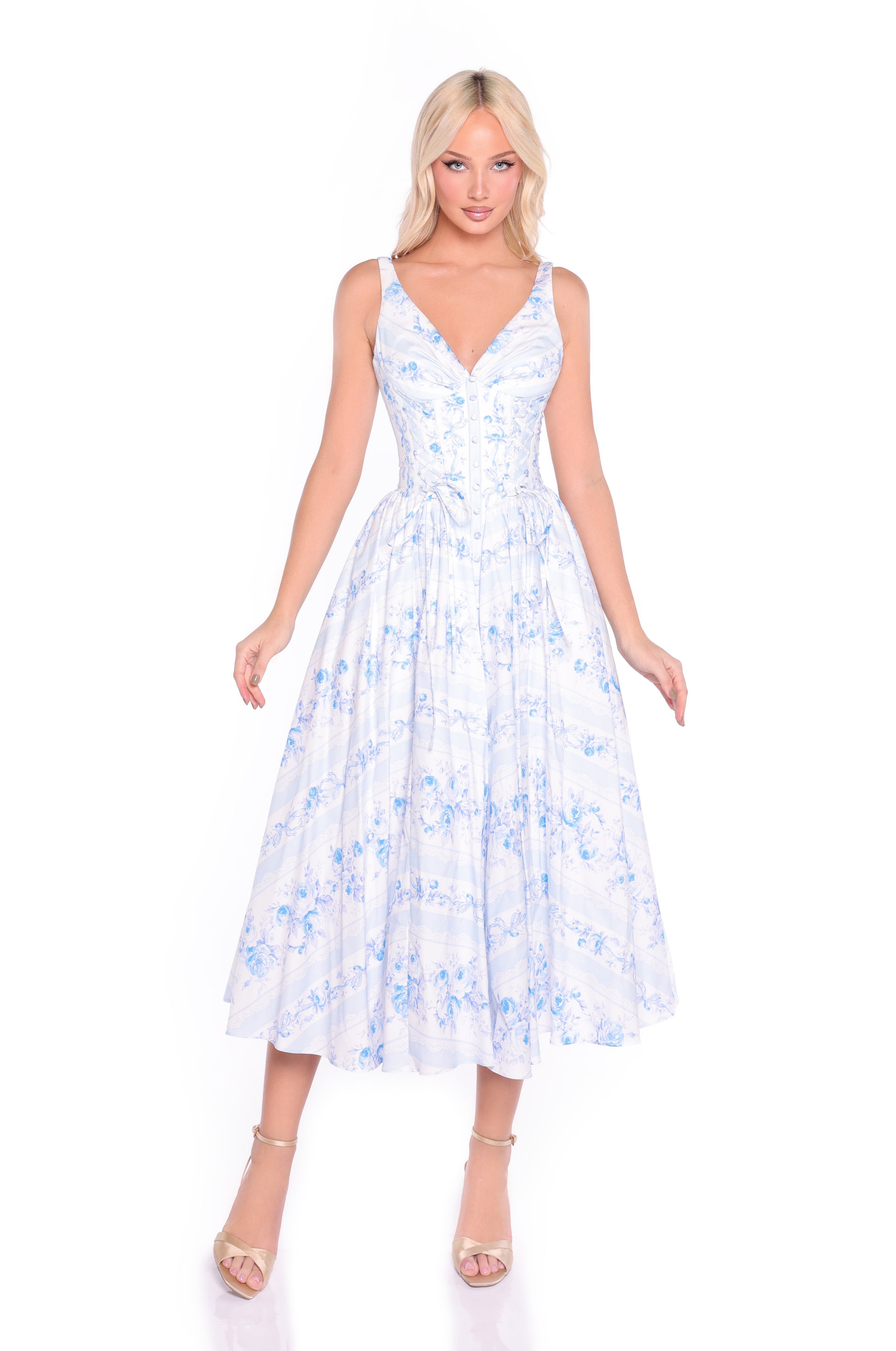 A woman wears the Ivory & Blue Print Summer Midi Casual Dress: Alina, featuring a sleeveless V-neck, fitted bodice, and flared skirt. The light blue and white floral midi dress is styled with light heels against a white background.